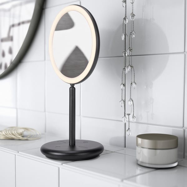 Et moderne forfængelighedsspejl med indbygget led-belysning sidder på en bordplade. Spejlet har en rund base og en usb-port til opladning.