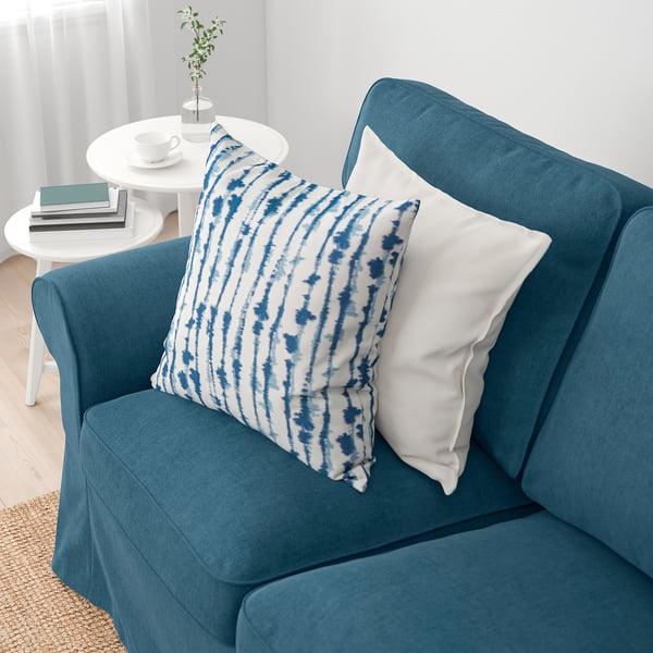 Blå sofa med blå og hvid pude, sidebord med bøger og kaffeopstilling.