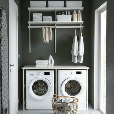 Moderne vaskerum med hvide UNIT-apparater, grønne vægge og organiserede hylder.