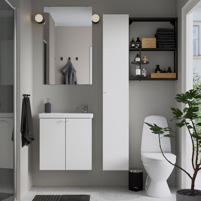 Moderne badeværelse med hvidt ENHET-vaskskab, flydende design, spejlet medicinskab, sorte detaljer, hvidt toilet, glasbruser og grøn plante.