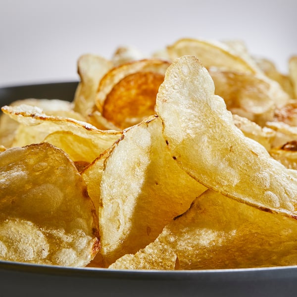 Sort skål med rustikke kartoffelchips med skind, let saltet. Sprød tekstur, gyldenbrun farve. Perfekt til fester eller snacks.