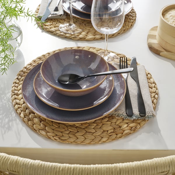 Borddækning med vævet dækkeserviet, rustikke fade, glas, bestik og stofserviet.