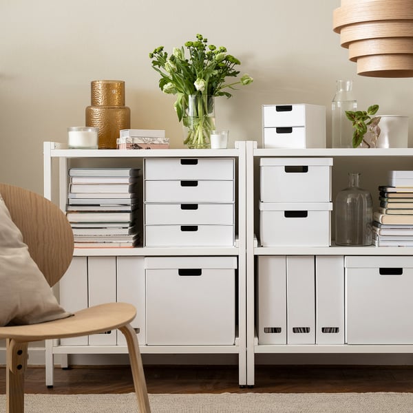 Hvide FJÄDERHARV-kasser på hylder, der rummer bøger, blomster og indretning. Ideel til arbejdsplads og stue, der blander funktionalitet og moderne design.