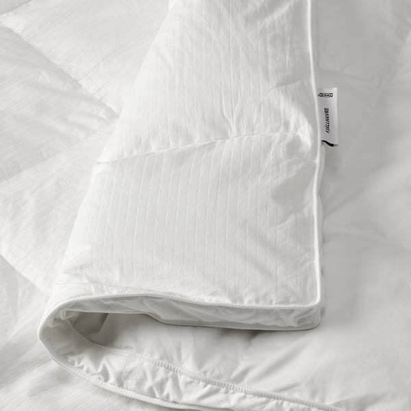 En fluffy hvid dyne på en seng med et mærke, der viser mærket FJÄLLHAVRE, der indikerer blød, dunfyldt varme.