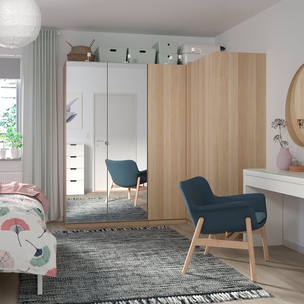 Et moderne soveværelse et FORSAND lyst træ garderobe, blå stol og skrivebord med gennemsigtige gardiner, der tillader blødt lys ind.