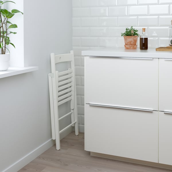 Rent køkken med hvidt skab, skuffe og stigestol mod væg; planter og flaske på disk.