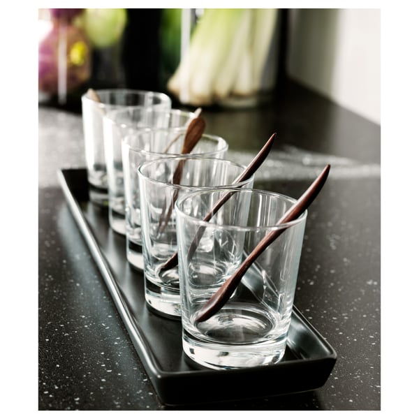 Enkle, klare GODIS-glas på sort bakke med spisepinde i træ, perfekt til cocktails eller desserter.