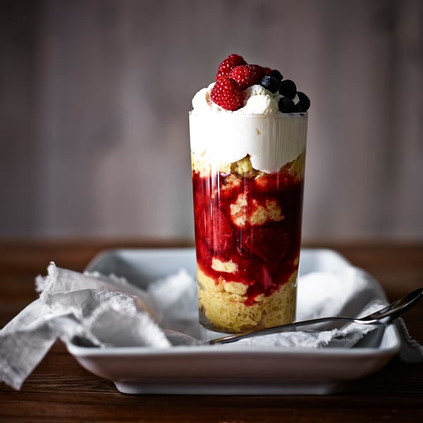 Høj dessertkop i glas fyldt med lag kage, fløde og bær; Perfekt til søde sager.