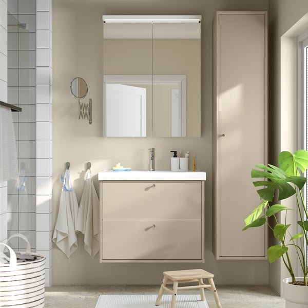 Moderne beige HAVBÄCK-vaskebord med stort skab, spejl, håndklæder, plante.