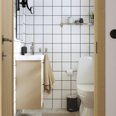 Et moderne badeværelse med en hvid flisevæg, sorte accenter og beige håndklæde. Minimalistisk design med rene linjer og kontrasterende farver.