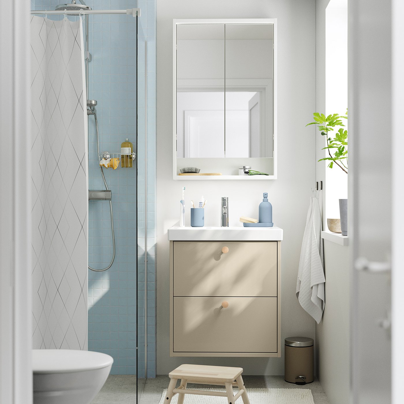 Moderne badeværelse med HAVBÄCK beige forfængelighed, lyseblå fliser, hvid håndvask, glasbruser og lille plante.