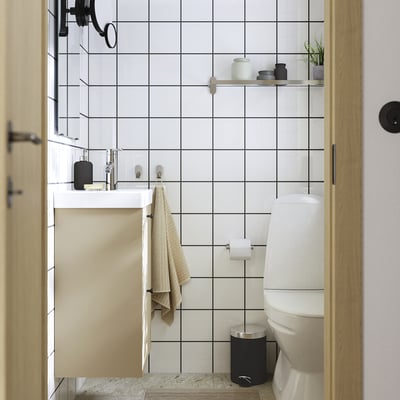 Moderne badeværelse med HAVBÄCK vægskab, hvid og beige, over toilet, sorte detaljer, enkel indretning.