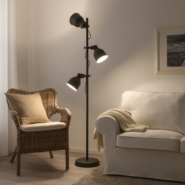 HEKTAR gulvlampe, sort, industrielt design, store metalskærme, justerbar højde, står højt ved siden af kurvestol og beige sofa.