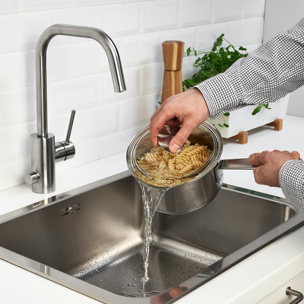 Person dræner pasta i køkkenvask med moderne sølvvandhane.