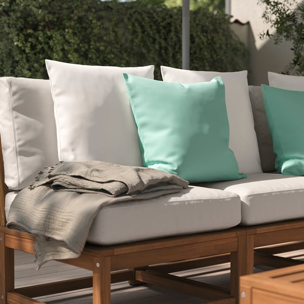 Udover udendørs terrassesofa med lysegrønne og hvide hynder og et beige tæppe.