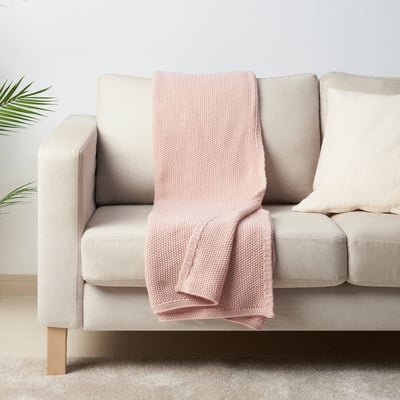 Lyserødt HUMLEMOTT tæppe på neutral sofa, blødt, strikket, hyggeligt, mellemstørrelse.