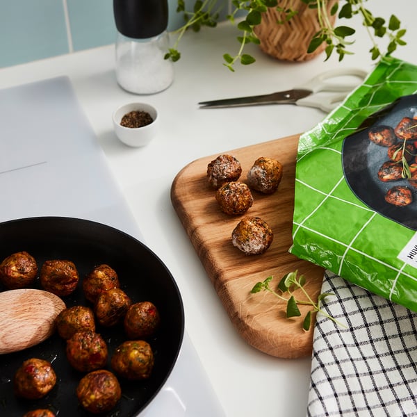Kogte frikadeller i pande, træplade, emballage siger HUVUDROLL med grøn farve, krydderurter, saltbøsse og hvid skål på køkkenbord.