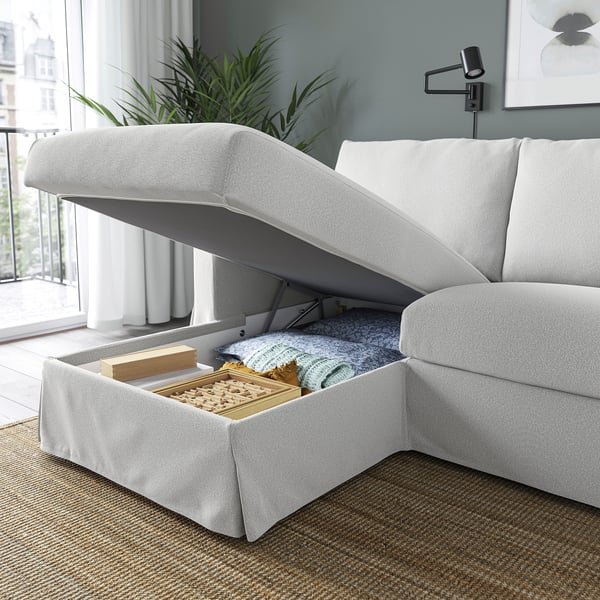 En moderne sofa med en chaiselong, der kan løftes op, afslører opbevaringsplads med tæpper og et brætspil indeni.