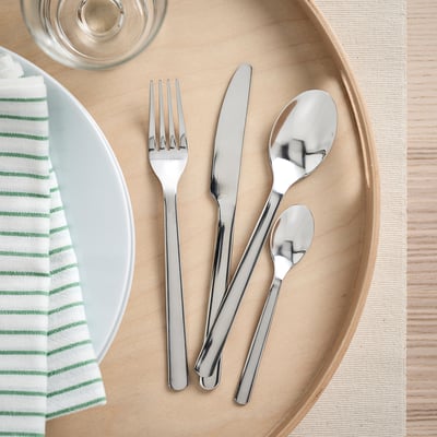 Bestik i rustfrit stål fra IKEA på et træfad med tallerken og serviet, minimalistisk design.