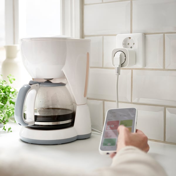 Et hvidt smart stik tilsluttet en hvid kaffemaskine på et køkkenbord.