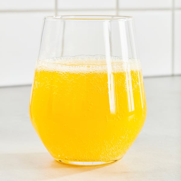 Klar glaskop fyldt med boblende, orangefarvet ISKUB-drik, placeret på en overflade. Nøgleingredienser: appelsinsmag, sødestoffer, lavt sukkerindhold.