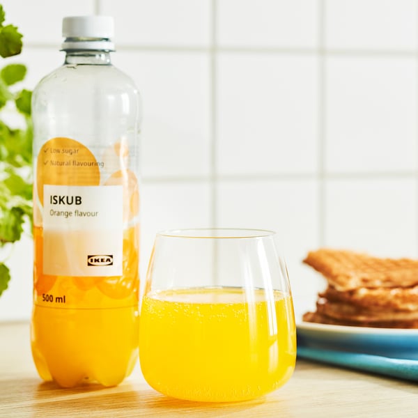 En flaske ikea-drik med appelsinsmag står ved siden af et glas fyldt med drikken på et træbord.