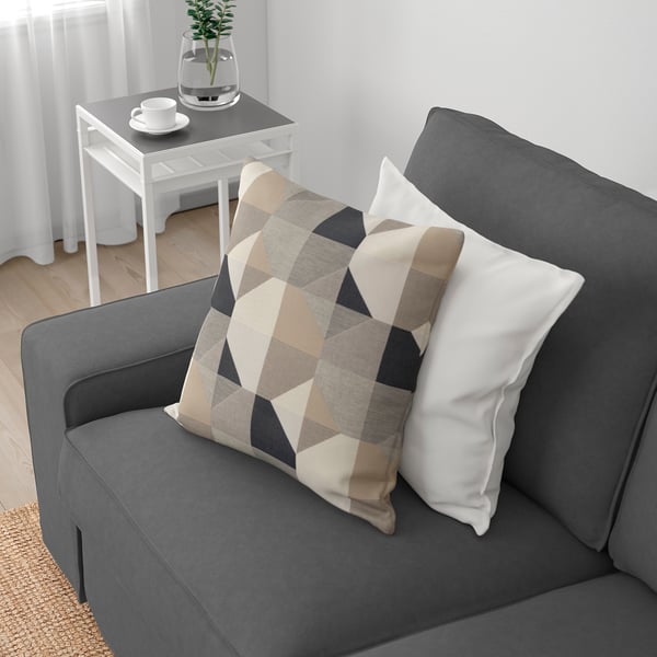 En grå sofa med tykke hynder og en mønstret pude. Et sidebord med en plante og kopper, der sandsynligvis er til kaffe, hvilket tyder på afslapning og komfort.