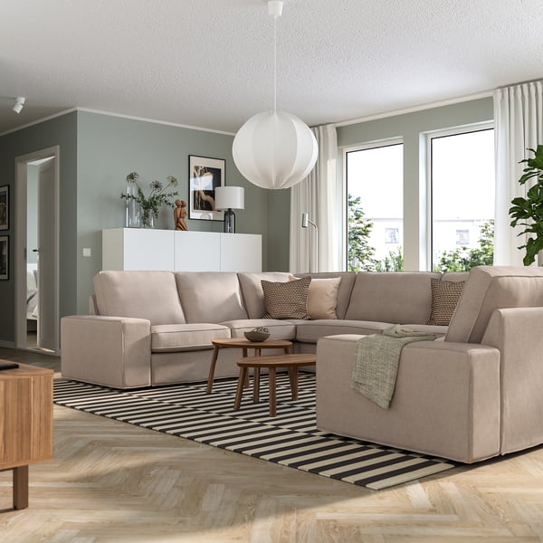 Moderne stue med KIVIK beige sofa, stribet tæppe, pendel og sidebord fra midten af århundredet. Sofaen er stor og har plads til flere sæder.