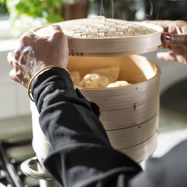Person, der holder bambusdamper over komfuret, koger runde dumplings. Sort ovnhandske bruges til beskyttelse.