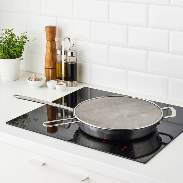 Rustfrit stål stænkskærm over sort komfur med håndtag og netoverflade.