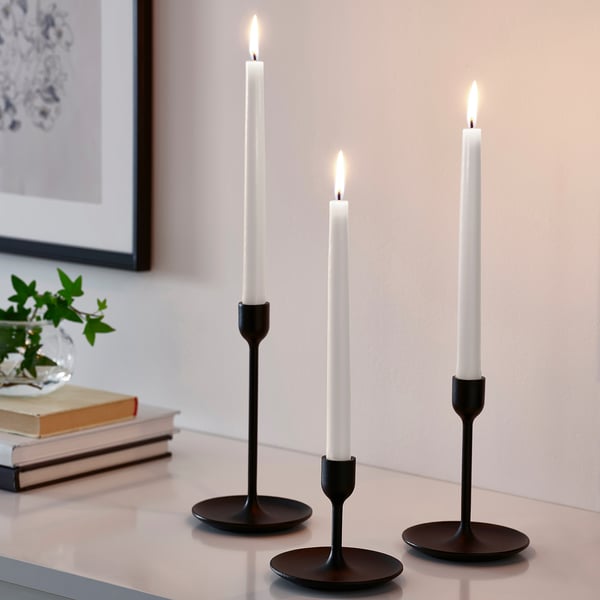 Tre KLOKHET sorte lysestager med hvide stearinlys. Slankt, cylindrisk design, lille størrelse i forhold til bøger og vase.