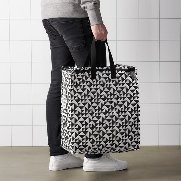 Person med stor KNALLA indkøbspose med geometrisk mønster. Tasken har håndtag og fremstår robust til dagligvarer eller vasketøj.