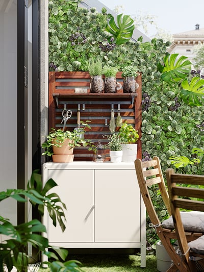 Styler udendørs miniskab, hvid, metal, rektangulær, enkelt design, grønne planter omkring.
