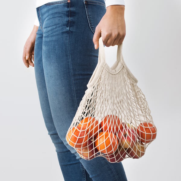 Person, der holder genanvendelig netpose fyldt med appelsiner, hvilket fremmer miljøvenlig shopping.