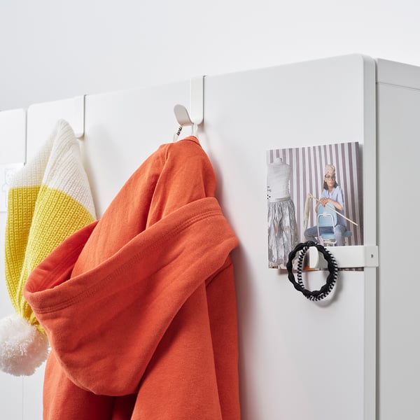 En hvid metalkrog med orange cardigan hænger på en hvid dør ved siden af en plakat af en kvinde, der stryger.