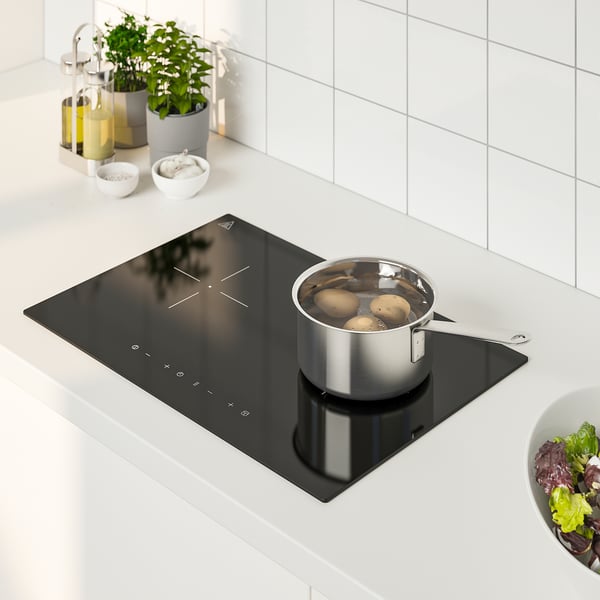 Lille sort induktionskomfur med pande, omgivet af køkkenartikler, herunder skåle, flasker og salatskål.