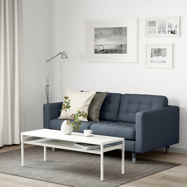 Minimalistisk stue: blå sofa med hvide puder, sofabord med vase og kop, sort-hvide fotos på væggen.