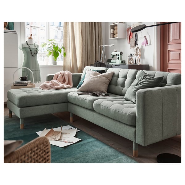 Moderne stue med LANDSKRONA l-formet sofa, lyserød/grå puder, grønt tæppe, symaskine.