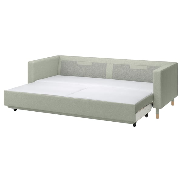 Moderne lysegrøn sovesofa med træben og plyspuder.
