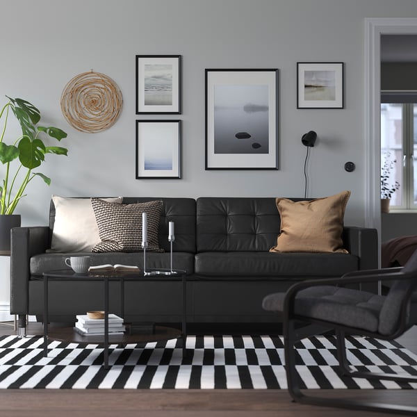 Moderne stue med sort sofa, tæppe, plante, kunst og sofabord.