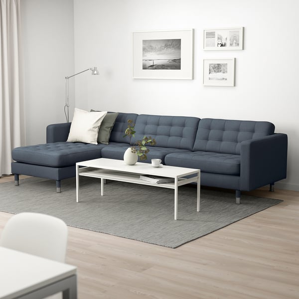 Moderne stue med blå l-formet sofa, hvidt sofabord, tæppe, gulvlampe og vægkunst.