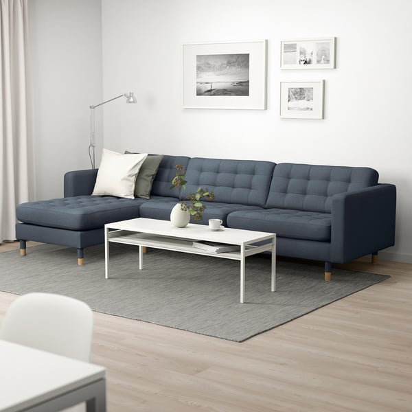 Moderne stue med mørkeblå l-formet sofa, hvidt sofabord og vægkunst.