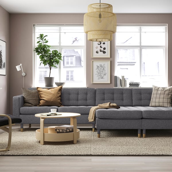 Grå LANDSKRONA sofa, træben, rundt sofabord. Flere puder, plante, stort vindue.