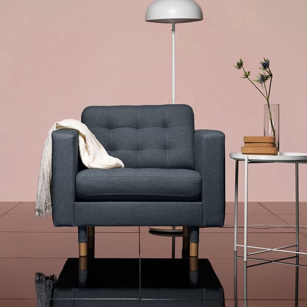 Hyggelig grå lænestol med træben ved siden af lille bord, lampe og blomster. Blødt, moderne design.