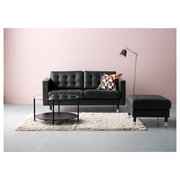 Moderne stue med sort lædersofa, sofabord i glas, gulvlampe og pjusket tæppe på lyserød væg.