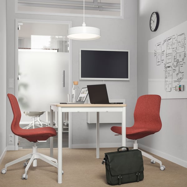 Lille hjemmekontor med LÅNGFJÄLL stol, bærbar computer, tv og whiteboard. Rød stol, sort taske, hvidt skrivebord, grå vægge.