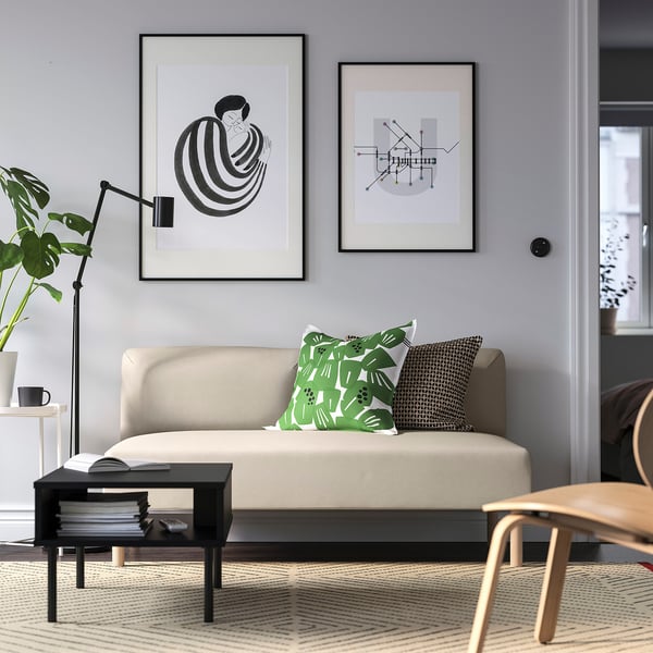 Moderne stue med lillem beige sofa, sort sofabord, to indrammede kunstarter og planter. Sofapuder i grøn og sort.