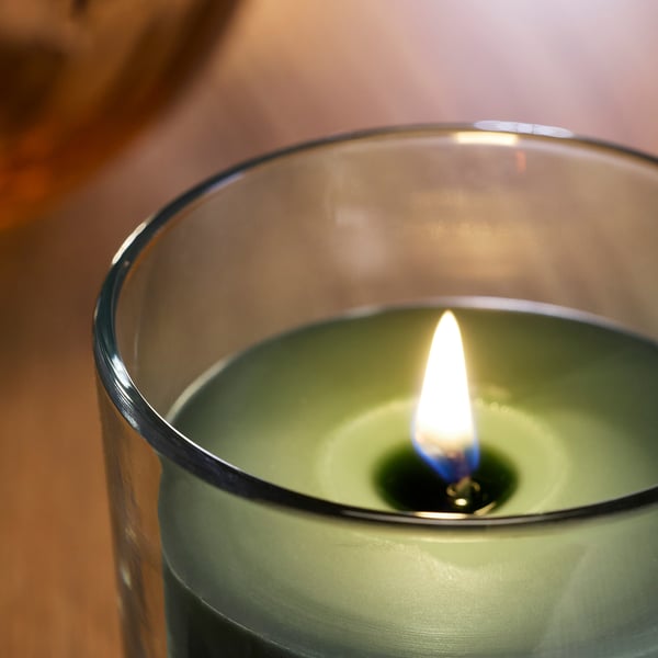 Nærbillede af et brændende grønt duftlys i en glasbeholder. Flammen flakker og kaster varmt lys.