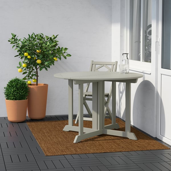Moderne terrasse med rundt LYDERSHOLM bord, stole, planter og citrontræ ved siden af en grå væg og hvidt vindue.