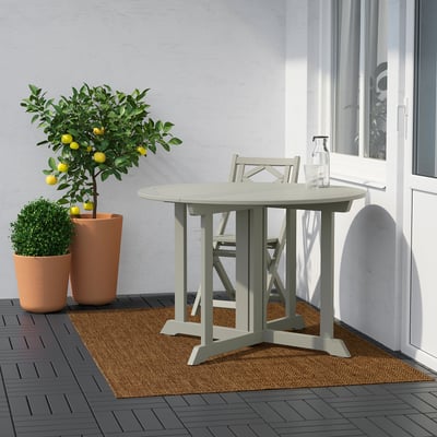 Moderne terrasse med rundt LYDERSHOLM bord, stole, planter og citrontræ ved siden af en grå væg og hvidt vindue.